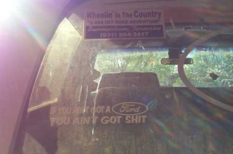 1988 Ford Bronco - Stickers on the rear window of a vehicle, including one with a Ford logo and a phone number.