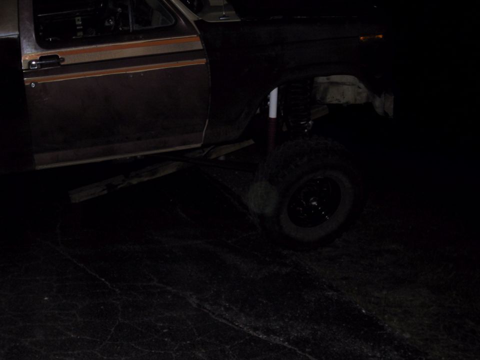 Night shot of a lifted brown 1980s Ford truck's front suspension with fender removed