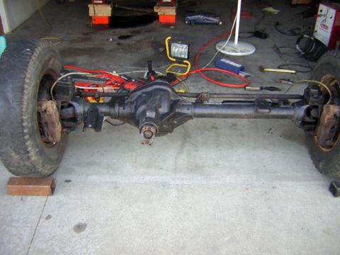 1995 Ford Bronco - Front axle assembly with tires and brake components is shown in a garage setting.