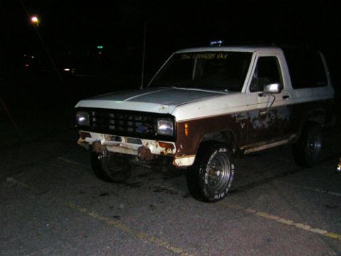 1986 Ford Bronco II - A weathered 1986 Ford Bronco II is parked at night, with visible rust on its body panels.