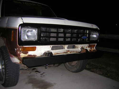 Night front-end view of a rusty white 1980s Ford SUV with black tube bumper