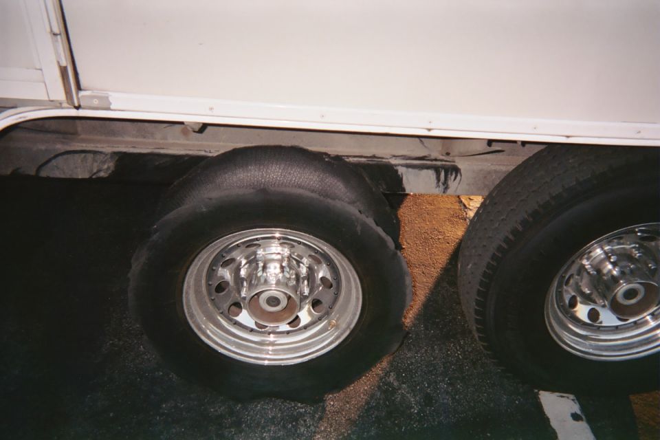 Flat shredded tire on chrome dually wheel under a white trailer or RV
