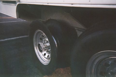 1990 Ford Bronco - Worn tires on chrome wheels under the side of a white trailer or RV, photographed in dim light.