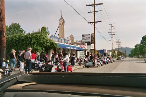 1968 Ford Mustang - A group of people and many scooters are gathered outside a shop on a street.