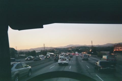 1990 Ford Bronco - Multiple lanes of freeway traffic at dusk viewed through a vehicle windshield, with hills and a sunset sky ahead.