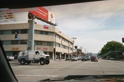 1990 Ford Bronco - white lifted cargo van with a star emblem on its door waits at a busy urban intersection beneath a billboard and storefronts.