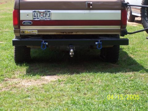 1987 Ford Bronco - The rear of a brown and white truck shows a custom bumper with tow hooks and a trailer hitch.