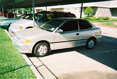1997 Ford Taurus - A silver coupe is parked under a carport, with other vehicles visible in the background.