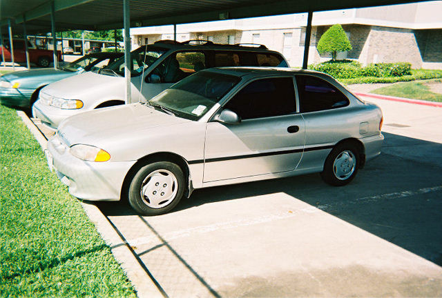 Silver coupe with tinted windows and black trim, parked under a carport next to other vehicles