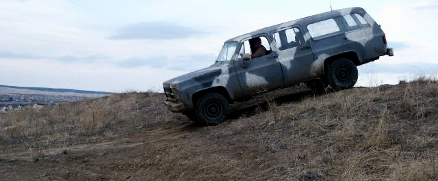Gray primer square-body Chevy Suburban driving down a grassy hill off-road