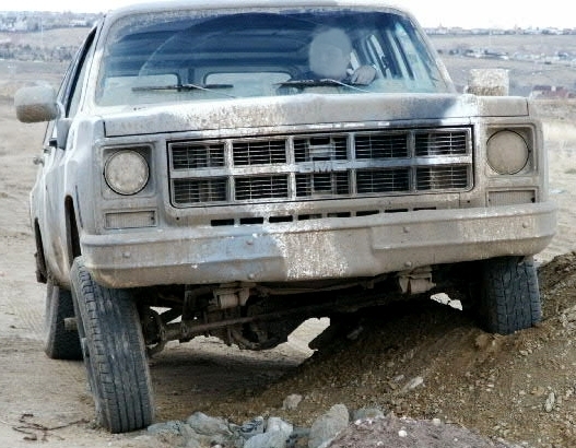 Dusty light-colored Chevy truck front end over a dirt mound off-road