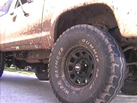 1984 Ford Bronco II - Close-up of a muddy SUV's side and tire, with visible text on the tire sidewall.