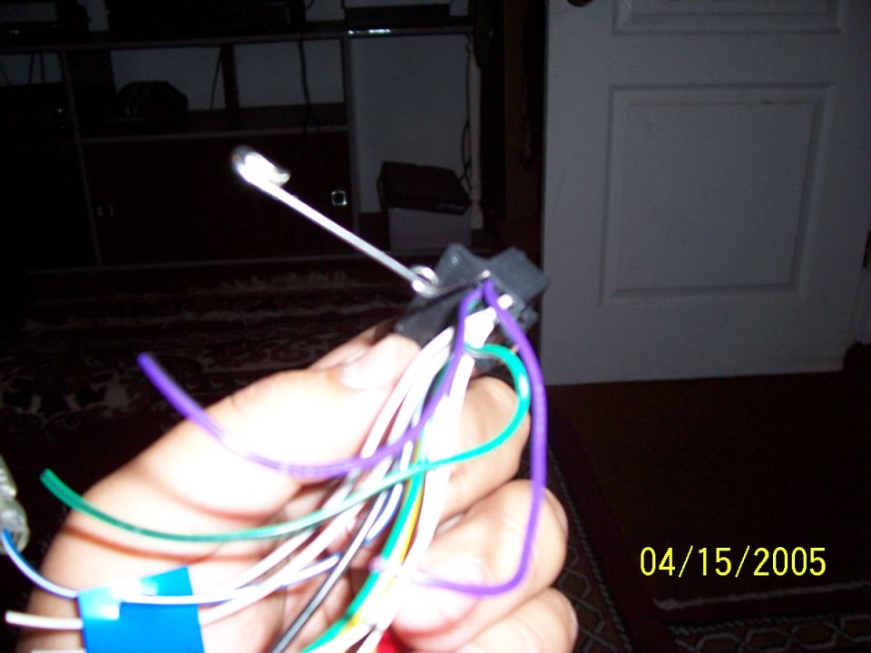 Hand holding a car stereo wiring harness with purple, green, and white wires