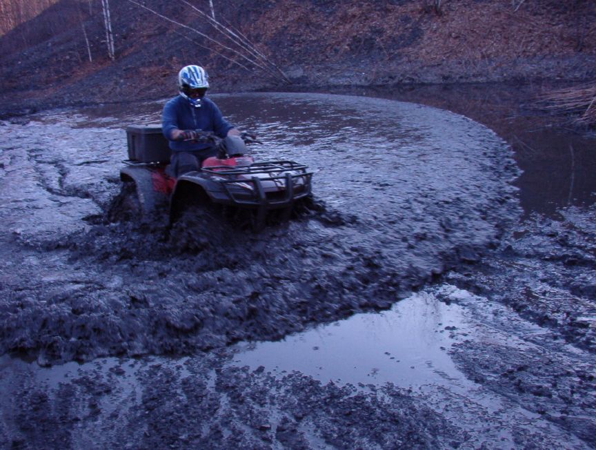Rider in blue jacket and helmet driving an ATV through deep churned mud