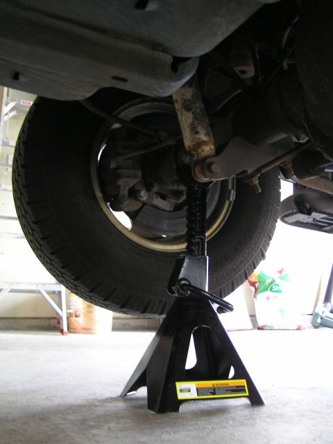 2000 Ford Excursion - The rear of a vehicle is raised on a jack stand for maintenance, showing the axle and suspension components.