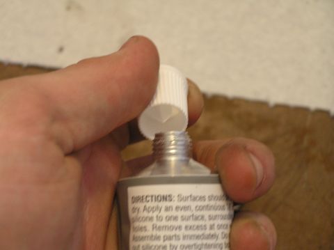 2000 Ford Excursion - A hand holds a tube of sealant, preparing to apply it to a surface.