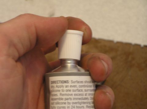 2000 Ford Excursion - A hand holds a tube of silicone sealant, showing the application directions on the label.