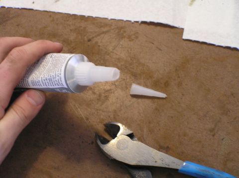 2000 Ford Excursion - A hand holds a tube of adhesive while a detached applicator tip and pliers rest nearby on a textured surface.