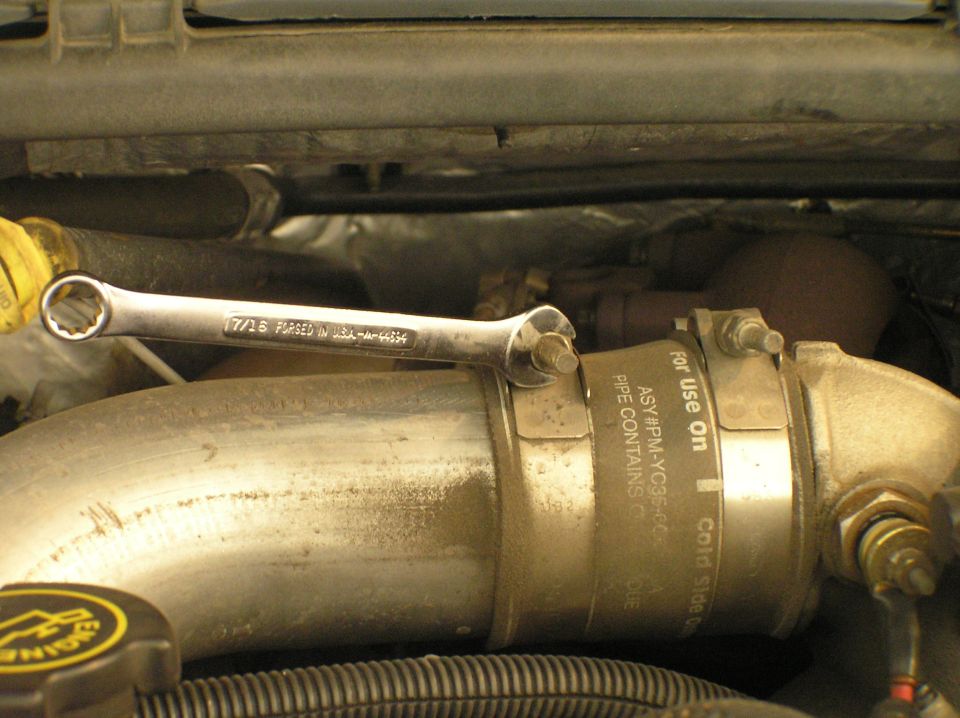 Chrome 7/16 wrench on labeled metal intake pipe with hose clamp in engine bay