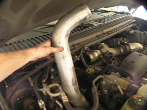 2000 Ford Excursion - A hand holds a large metal pipe, likely for a CAC hose replacement, within the engine bay of a 2000 Ford Excursion.