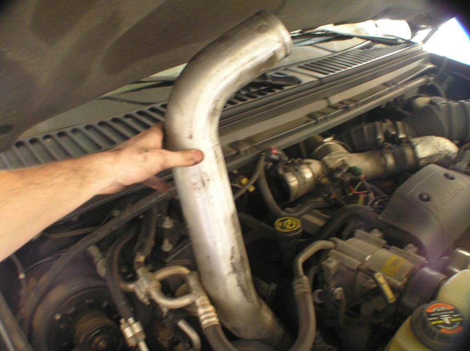 Hand holding curved metal intake pipe in an open engine bay