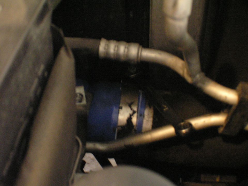 Blue-banded canister with metal lines and ribbed hose in dim engine bay