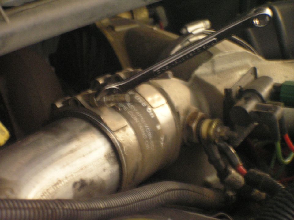 Wrench on a bolt near a metal engine canister with wiring and hoses