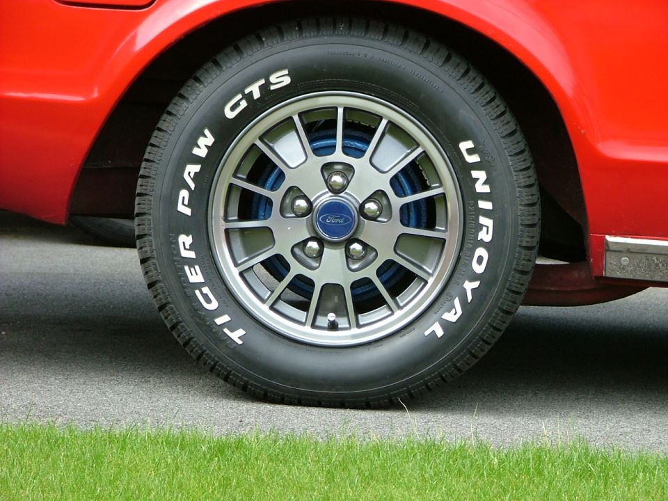 Red car's silver Ford alloy wheel with blue accents and Uniroyal Tiger Paw GTS white-letter tire