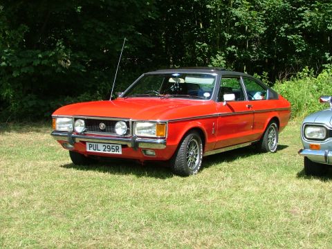 1976 Ford Granada - A red 1976 Ford Granada coupe is parked on a grassy field, with another vehicle partially visible to the right.