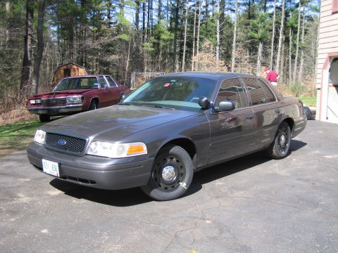 1991 Ford LTD Crown Victoria - A dark gray Ford Crown Victoria is parked on an asphalt driveway, with a maroon sedan in the background.