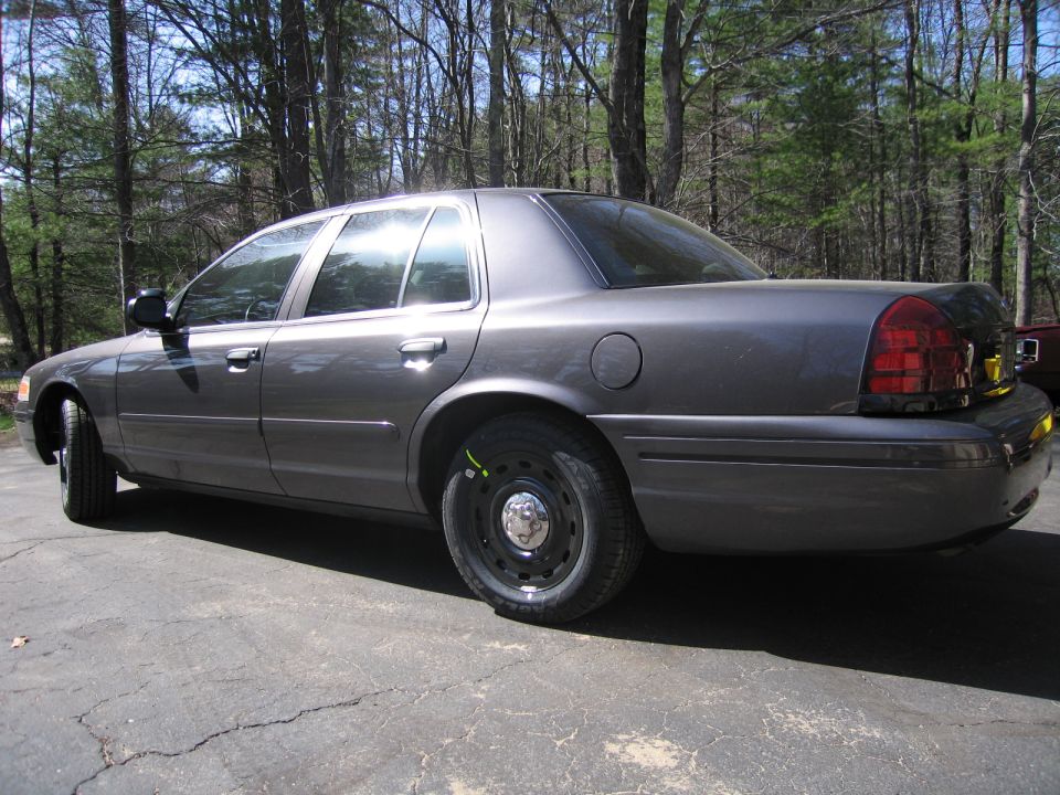 Gray sedan parked on cracked asphalt, side view, showing rear taillight and steel wheel
