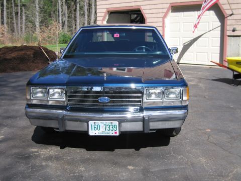 1991 Ford LTD Crown Victoria - A blue Ford Crown Victoria is parked in front of a garage with an American flag visible.