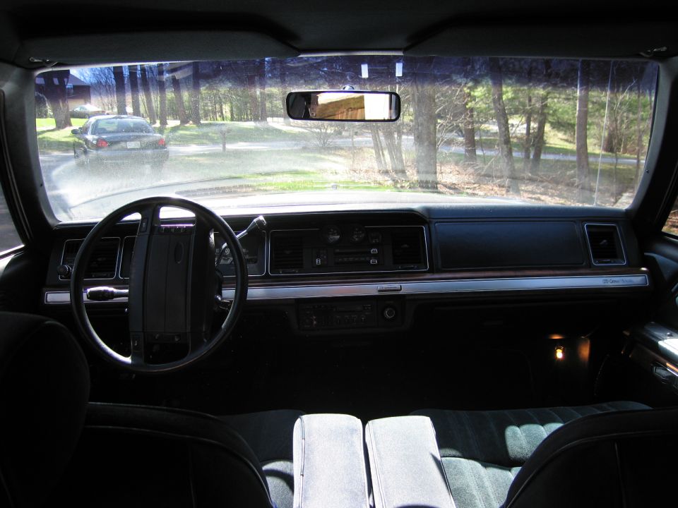 Interior view of a Ford Crown Victoria, looking out the windshield at another car on a tree-lined street