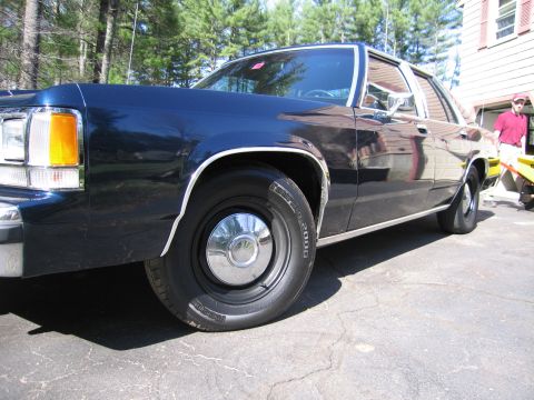 1991 Ford LTD Crown Victoria - A dark blue sedan is parked on a driveway with a house and trees visible in the background.