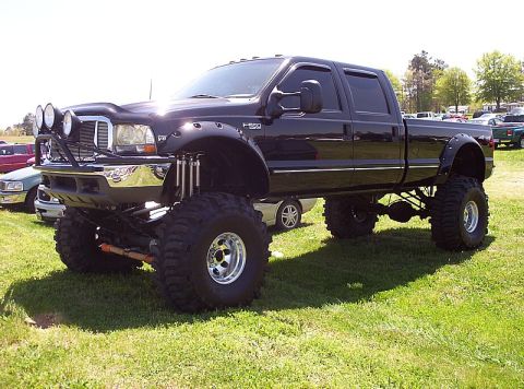 1995 Ford Bronco - A heavily modified black pickup truck is parked on a grassy field with other vehicles in the background.