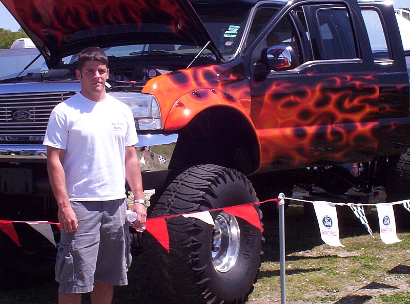 Black lifted truck with orange flame decals, large off-road tires, and an open hood