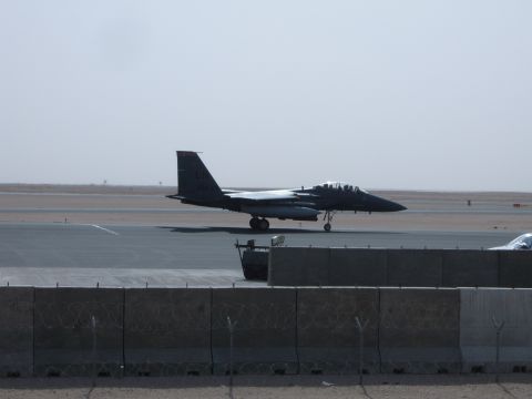 1988 Ford Bronco - A military jet is on the tarmac, with a barrier in the foreground and a hazy sky in the background.