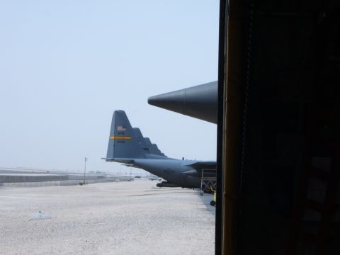 1988 Ford Bronco - A line of gray military cargo planes are parked on a sandy airfield, viewed from an open doorway.
