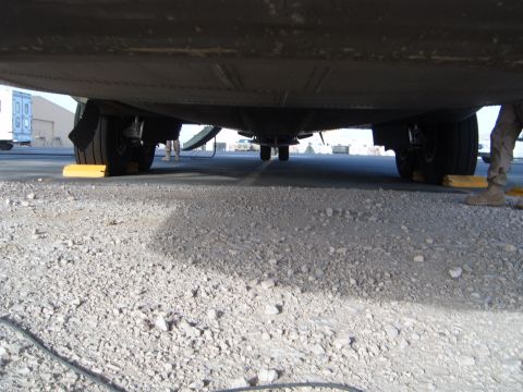 1988 Ford Bronco - The underside of a vehicle is visible, supported by yellow wheel chocks on a gravel surface.