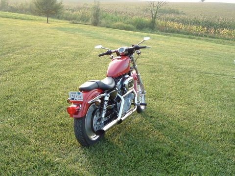 2002 Harley-Davidson Sportster Custom - A red motorcycle is parked on a grassy field with a cornfield in the background.