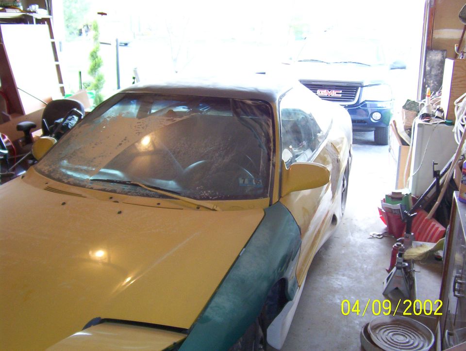 Yellow car in garage, 3q-front view. Another vehicle visible in background