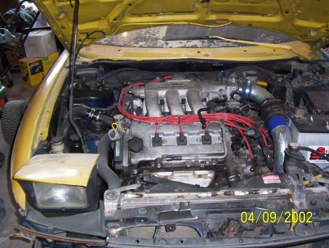 1994 Ford Probe - The engine bay of a yellow car is shown, a V6 engine and red spark plug wires. A date stamp indicates the photo was taken on 04/09/2002.
