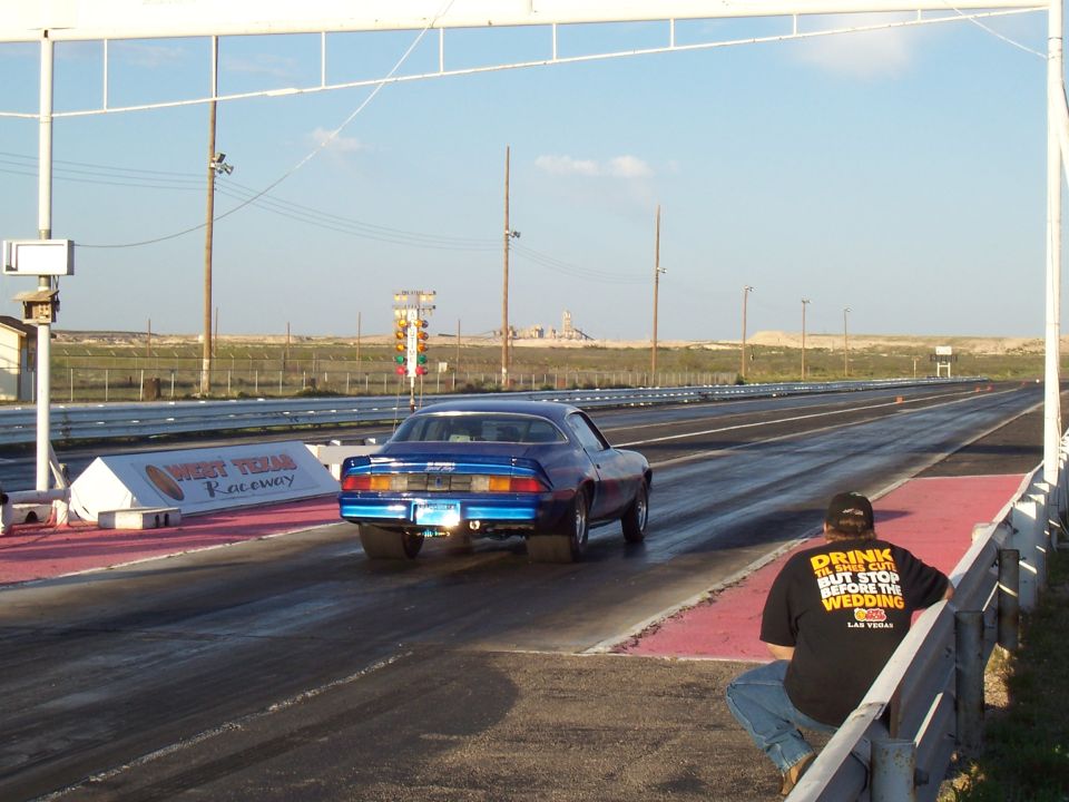 Blue muscle car with wide rear tires on a drag strip, rear view