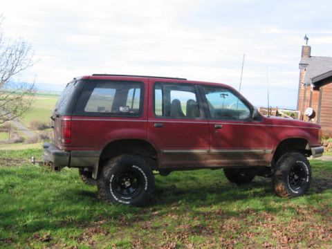 1991 Ford Explorer - This red 1991 Ford Explorer is seen from the side, parked on a grassy hill with a house in the background.