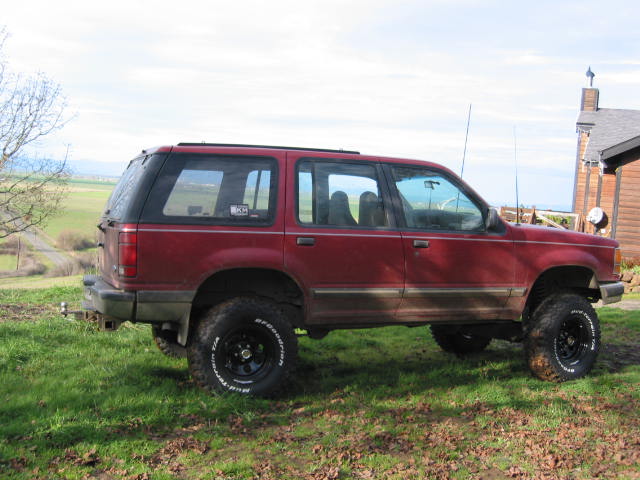 Red 1991 Ford Explorer side view, parked on grass with a house in background