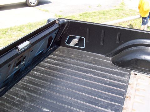 1969 Ford Ranchero - The interior of a black pickup truck bed is shown, with a cat visible through a small opening in the side panel.