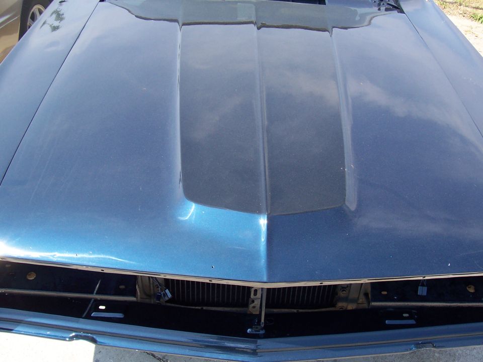 Metallic blue car hood with twin ridges, front grille visible below