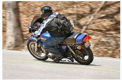 1985 Ford LTD Crown Victoria - Rider on a blue Suzuki motorcycle navigates a road with wooded hills in the background.
