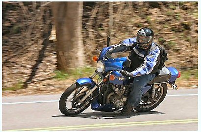 1985 Ford LTD Crown Victoria - A rider navigates a road on a blue motorcycle, with trees lining the route.