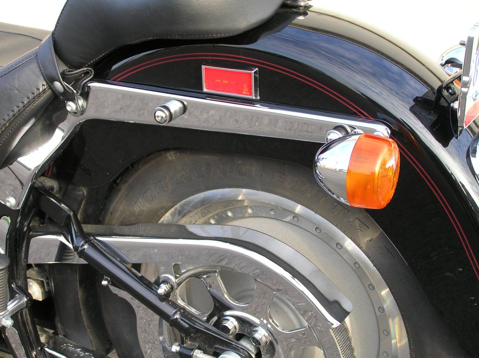 Rear of black Harley motorcycle with chrome bracket, amber turn signal, and tire.